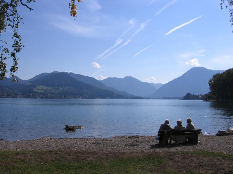 Drei Menschen sitzen am Seeufer vor einer Berglandschaft