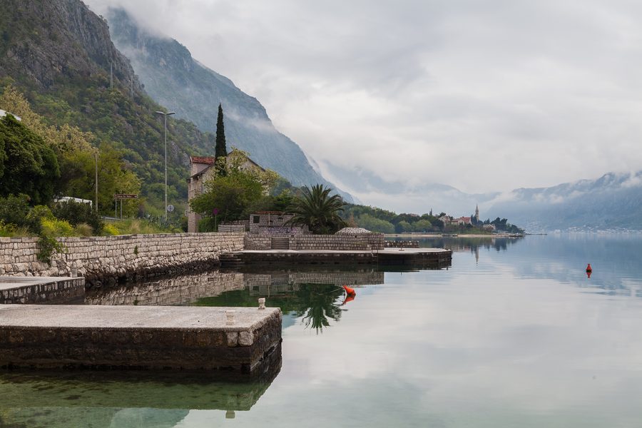Uferort Ljuta an der Bucht von Kotor mit Wasser und steilen Bergen im Hintergrund.